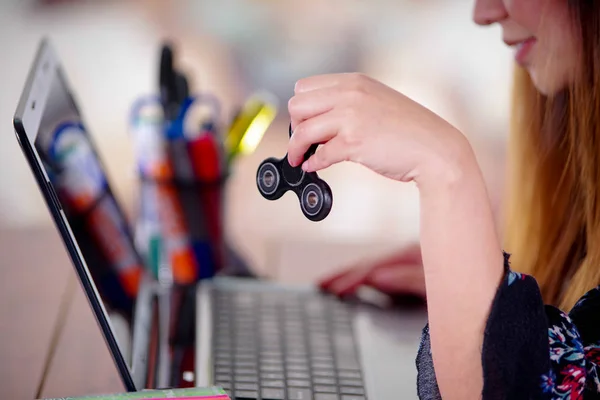 Ung kvinna håller en populära fidget spinner leksak i handen medan hon arbetar i sin dator på kontoret bakgrund — Stockfoto