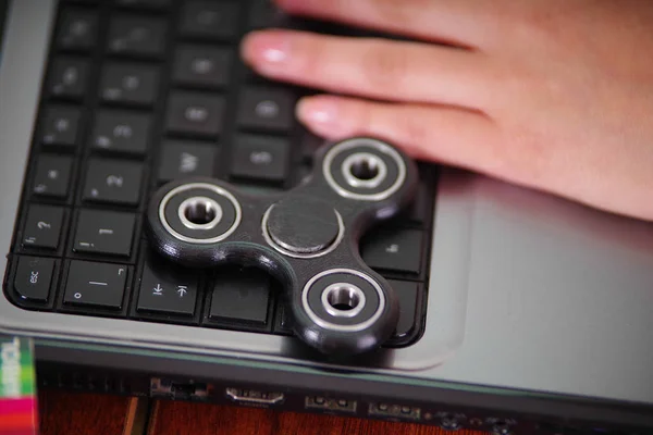 Jovem mulher trabalhando no computador e um brinquedo popular fidget spinner sobre o laptop, no fundo do escritório — Fotografia de Stock