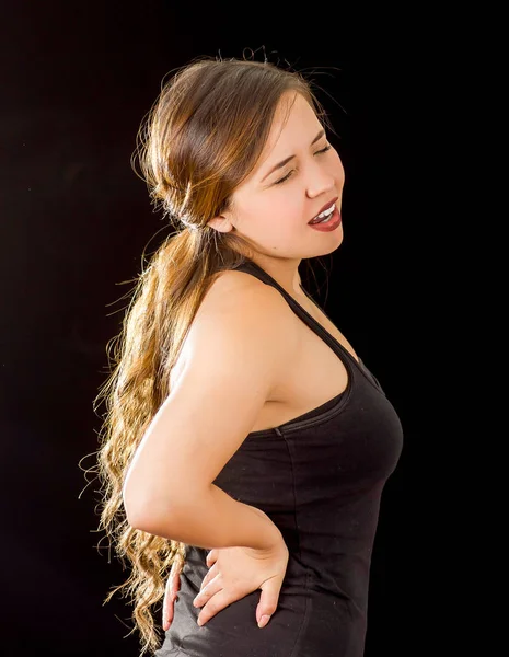 Young beautiful sportwoman suffer cervical pain in her lower back, in black background — Stock Photo, Image