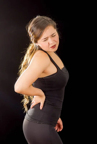 Young beautiful sportwoman suffer cervical pain in her lower back, in black background — Stock Photo, Image