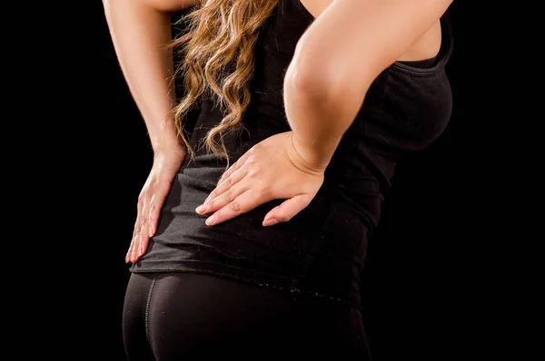 クローズ アップ若い美しい sportwoman の黒の背景で彼女のより低い背部で頸の痛みに苦しむ — ストック写真