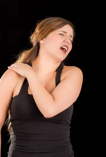 Mulher bonita sofre de dor no ombro em um fundo preto — Fotografia de Stock