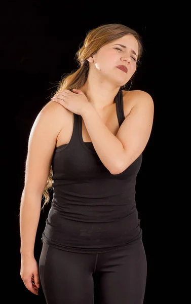 Beautiful young woman suffer from shoulder pain in a black background — Stock Photo, Image