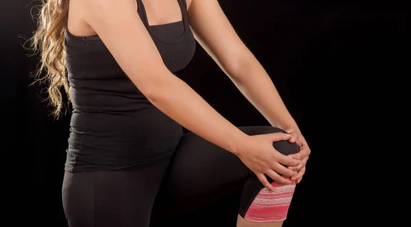 Gros plan d'une belle jeune femme sportive séduisante tenant un genou blessé souffrant de douleur, en fond noir — Photo