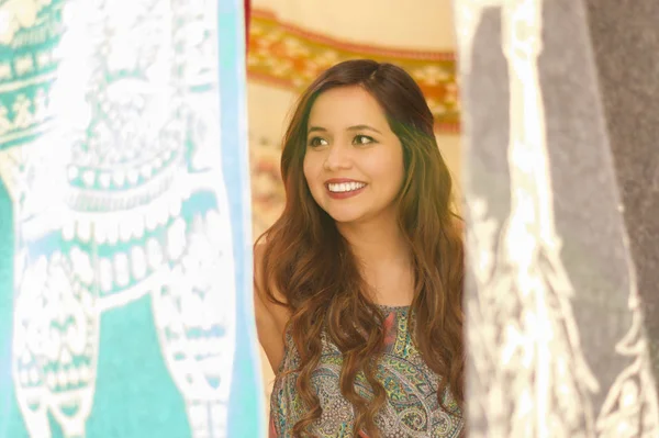 Gros plan d'une belle jeune femme souriante se cachant derrière le fil textile de vêtements traditionnels andins et tissé à la main en laine, fond de tissus colorés — Photo
