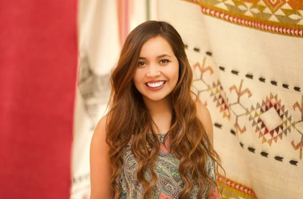 Hermosa joven sonriente posando frente a una ropa tradicional andina, telas coloridas fondo — Foto de Stock