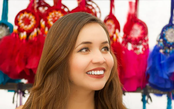 Close up de uma bela jovem sorridente olhando para a horizontal na frente de catchdreamers coloridos borrados, em fundo colorido do mercado — Fotografia de Stock
