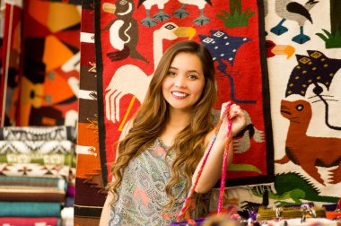 Bir and geleneksel çanta tutarak ve renkli kumaşlar arka plan ile kamera için poz güzel gülümseyen genç kadın