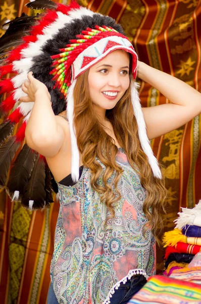 Une belle jeune femme portant une plume de chapeau amérindienne. avec fond de tissus colorés — Photo