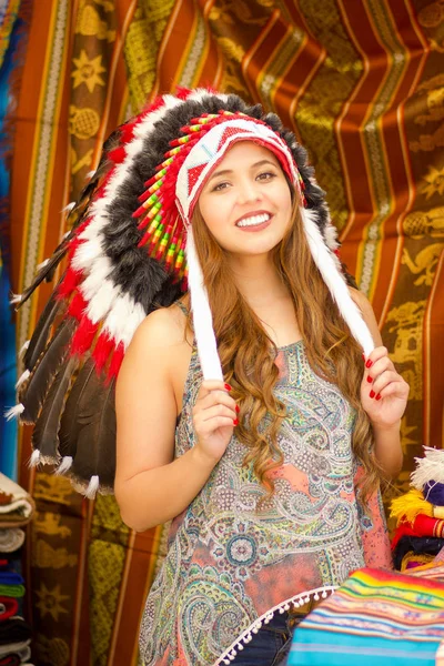 Uma bela jovem mulher usando penas de chapéu nativo americano. com fundo de tecidos coloridos — Fotografia de Stock