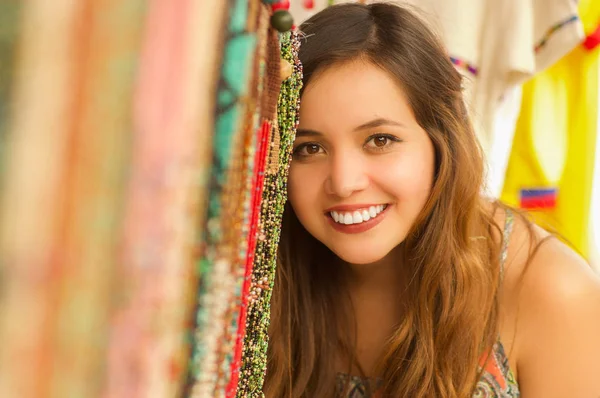 Nahaufnahme einer schönen lächelnden jungen Frau, die sich hinter dem traditionellen Textilgarn der Anden versteckt und von Hand in Wolle gewebt wird, farbenfroher Stoffhintergrund — Stockfoto
