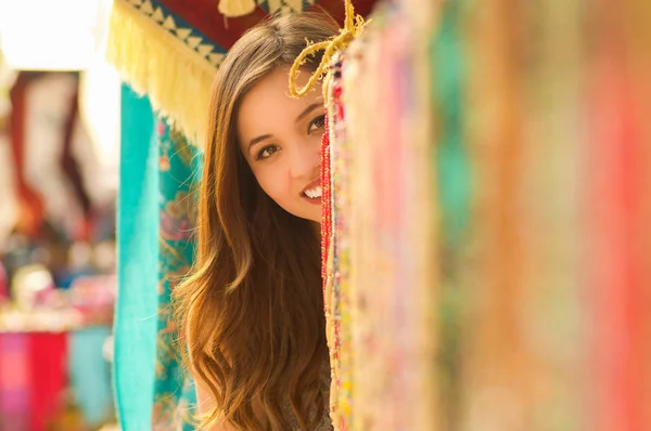 Primer plano de una hermosa joven sonriente escondida detrás del hilo textil tradicional andino y tejida a mano en lana, telas coloridas fondo —  Fotos de Stock