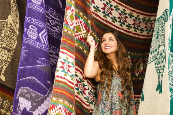 Krásná usměvavá mladá žena dotýká andské tradiční oděvy a pózuje pro kamery, barevné tkaniny pozadí — Stock fotografie
