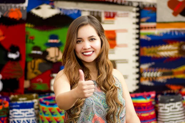 Vackra leende ung kvinna med humbs upp och poserar för kameran, med färgglada Andinska traditionella kläder tyger bakgrund — Stockfoto