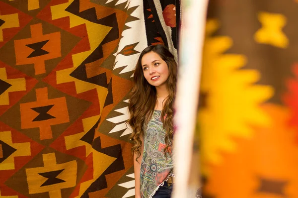 Bonita sorridente jovem mulher tocando andino roupas tradicionais e posando para câmera, fundo tecidos coloridos — Fotografia de Stock