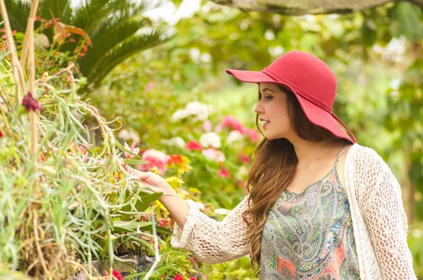 Fröhliche junge Frau, die draußen im Garten steht und einen roten Hut im Garten trägt — Stockfoto