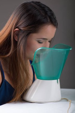 Genç kadının bir tıbbi Buharlaştırıcı Nebulizatör makinede gri arka plan ile enhalasyon yapması