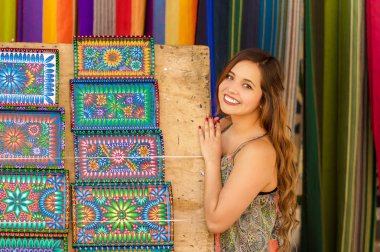 Güzel gülümseyen genç kadın and dokunmadan geleneksel Giyim Tekstil iplik ve dokuma tarafından el yün, renkli kumaşlar arka planda