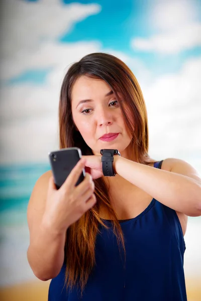 Mulher de negócios vestindo em seu pulso um relógio inteligente com controle de voz e usando seu celular, em um fundo dia ensolarado — Fotografia de Stock