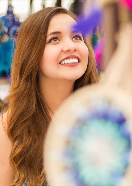 Κοντινό πλάνο του μια όμορφη χαμογελαστή νεαρή γυναίκα που ψάχνει ένα πολύχρωμο παραδοσιακές catchdreamers των Άνδεων, στην πολύχρωμη αγορά υφασμάτων φόντο — Φωτογραφία Αρχείου