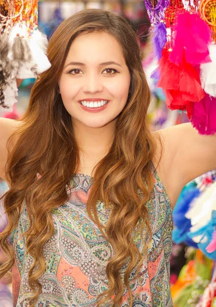 Belle jeune femme souriante se cachant derrière un attrapeur coloré, dans fond de tissus de marché colorés — Photo