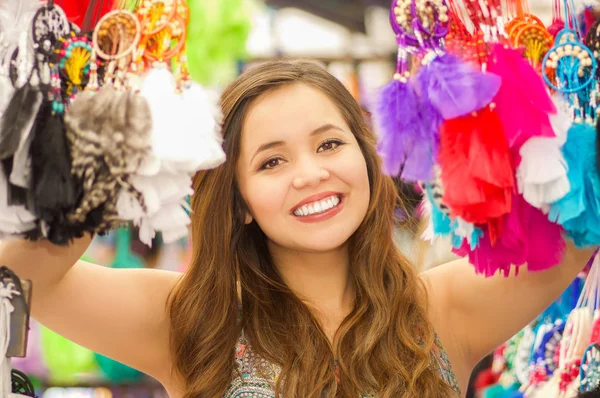 Close-up de uma bela jovem sorridente escondendo atrás de um coletor colorido, em fundo de tecidos coloridos do mercado — Fotografia de Stock