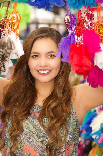 Bela sorrindo jovem mulher escondida atrás de um coletor colorido, no mercado colorido tecidos fundo — Fotografia de Stock