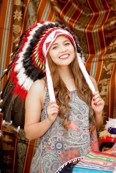 Une belle jeune femme portant une plume de chapeau amérindienne. avec fond de tissus colorés — Photo