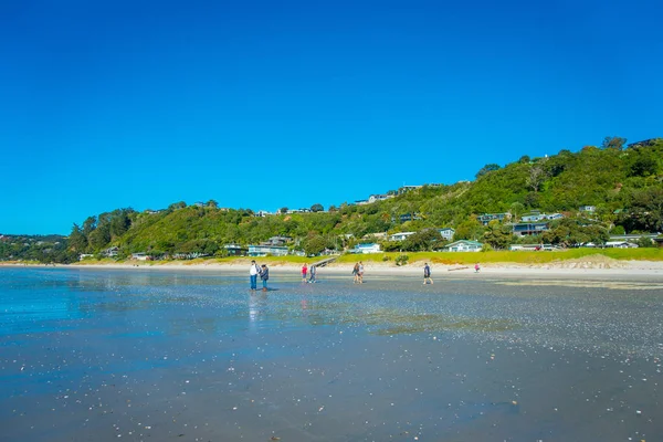 AUCKLAND, NUEVA ZELANDA - 12 DE MAYO DE 2017: Un pueblo no identificado caminando por la playa de arena oscura en la isla de Waiheke, Nueva Zelanda, con un hermoso cielo azul en un día soleado — Foto de Stock