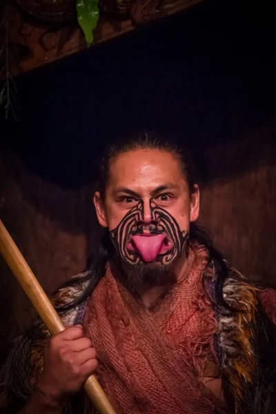 NORTH ISLAND, NEW ZEALAND - MAY 17, 2017: Maori man sticking out tongue with traditionally tatooed face and in traditional dress at Maori Culture, Tamaki Cultural Village, Rotorua, New Zealand — стоковое фото
