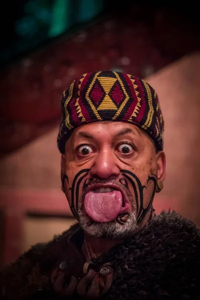 北の島, ニュージーランド-2017 年 5 月 17 日: 玉木文化村、マオリの帽子をかぶってマオリ文化で伝統的な衣装で伝統的刺青顔で舌を突き出してマオリ人のクローズ アップ — ストック写真