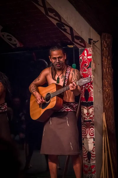 NORTH ISLAND, New ZEALAND- 17 พฤษภาคม ค.ศ. 2017: ใกล้ชิดกับชายชาวทามากิมาโอริที่มีใบหน้าที่มีรอยสักแบบดั้งเดิมและในชุดประเพณีที่วัฒนธรรมโมริ เล่นกีตาร์ในหมู่บ้านวัฒนธรรมทามากิ, โรโตรัว — ภาพถ่ายสต็อก