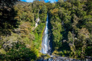 Billy Falls kayaların üzerinden akan buzul mavi nehir su ile. Haast Pass, South Island, Yeni Zelanda