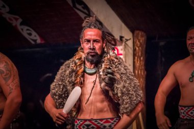 North Island, Yeni Zelanda - 17 Mayıs 2017: ahşap mızrak, geleneksel olarak dövmesi ile tutarak ciddi Tamaki Maori adam karşı karşıya, Maori kültürüne, New Tamaki kültür köyde giyen geleneksel kıyafet