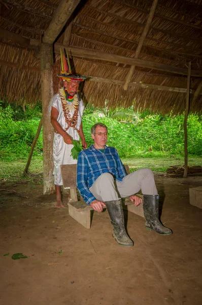 LAGO AGRIO, ÉQUATEUR - 17 NOVEMBRE 2016 : Shaman siona en costume traditionnel avec un chapeau de plumes dans un village indigène de la réserve faunique de Cuyabeno dans un rituel spirituel avec un touriste — Photo