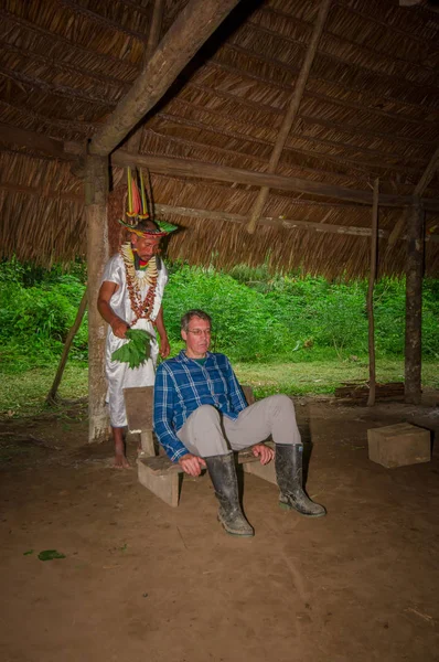 LAGO AGRIO, ECUADOR - 17 DE NOVIEMBRE DE 2016: Chamán de Siona en traje tradicional con sombrero de plumas en un pueblo indígena de la Reserva de Vida Silvestre Cuyabeno en un ritual espiritual con un turista — Foto de Stock