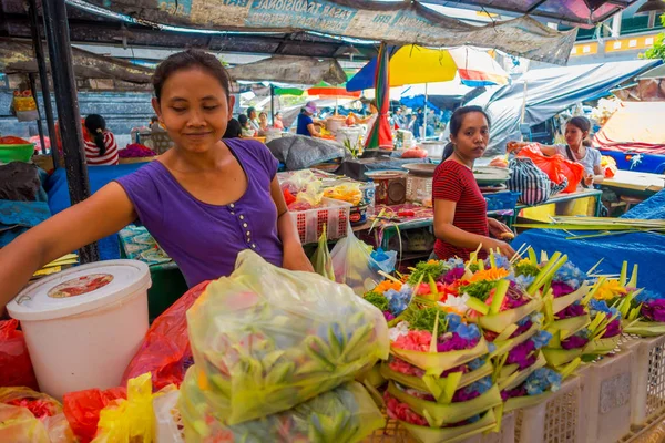 BALI, INDONESIA - 08 DE MARZO DE 2017: Mujer no identificada hace un arreglo de flores dentro de una caja hecha de hojas en un mercado, sobre una mesa, en la ciudad de Denpasar en Indonesia —  Fotos de Stock