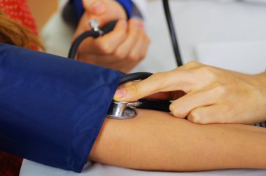 Bir kadın ile bir tensiometer onu kolundan Oda arka plan danışmanlık doktor sırasında darbe duymak steteskop kullanarak genç bir doktorun yakın çekim