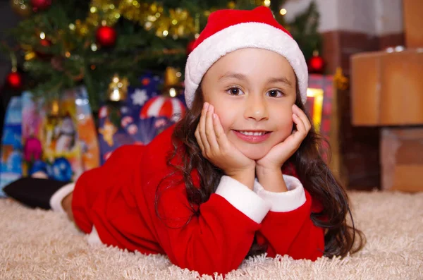 Hermosa niña sonriente usando una ropa de Navidad con un fondo de árbol de Navidad con algunos regalos — Foto de Stock