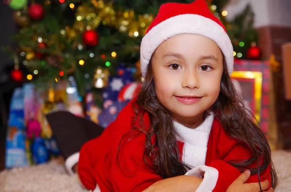 Mooi lachende litle meisje dragen van een kerst kleding met de achtergrond van een kerstboom met sommige presenteert — Stockfoto