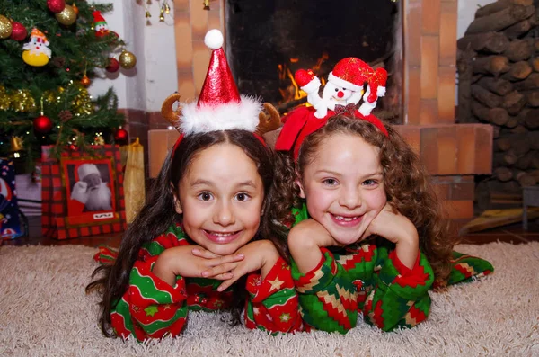 실내 chimmey 배경 흰색 카펫에 누워 크리스마스 옷을 입고 두 아름 다운 웃는 저 작은 여자의 클로즈업 — 스톡 사진