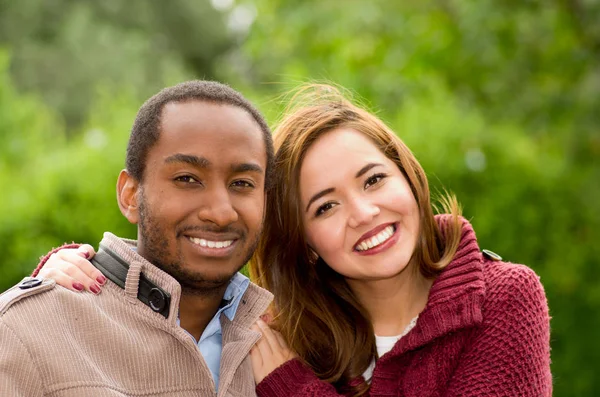 Hermosa y sonriente feliz pareja joven interracial mirando a la cámara en el parque al aire libre — Foto de Stock