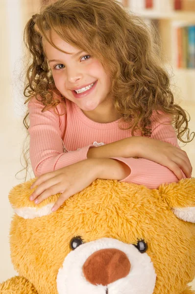 Un retrato de una jovencita bonita sonriendo y posando sobre la cabeza de su osito de peluche en un fondo de consultorio médico —  Fotos de Stock