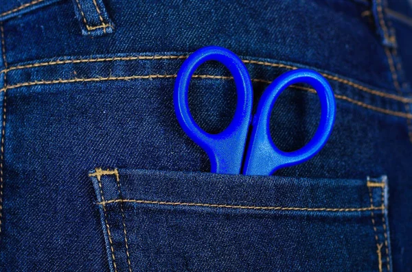 Blue scissors inside of jeans back pocket with a hand