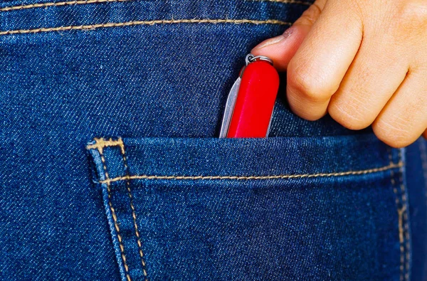 Woman hand putting a swiss knife inside of jeans back pocket — Stock Photo, Image