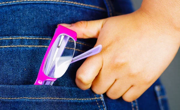 Woman hand holding a pink glasses inside of jeans back pocket — Stock Photo, Image