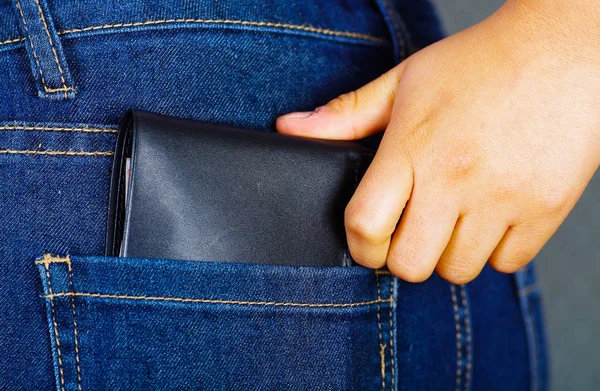 Mano de mujer poniendo una billetera negra dentro del bolsillo trasero de los pantalones vaqueros —  Fotos de Stock