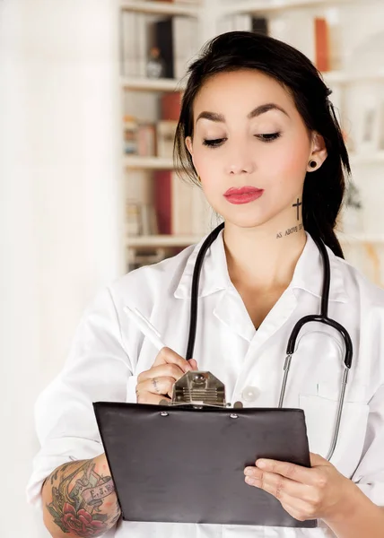 Beautiful tattooed young doctor in office background — Stock Photo, Image