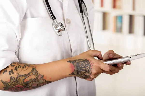 Primo piano di un giovane medico tatuato che tiene tra le mani una tavoletta che legge i risultati medici dei pazienti, in ufficio — Foto Stock