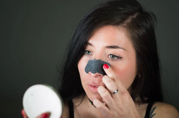 Bellezza giovane donna guardando specchio un aplying una maschera naso nero per pulire la pelle da macchie nere — Foto Stock